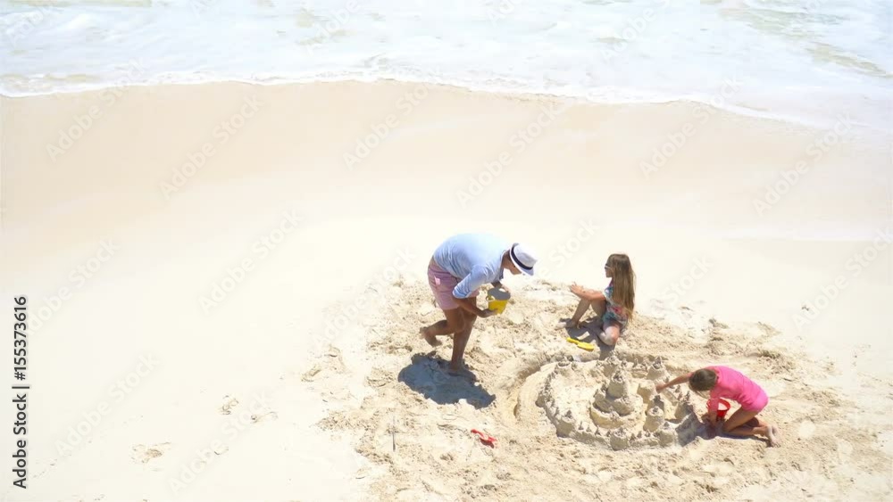 View from above to father and little daughters making sand castle at tropical beach View from above to father and little daughters making sand castle at tropical beach