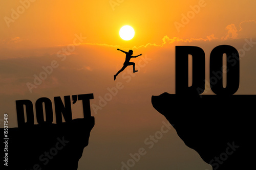 Man jumping from don't to do text over cliff on sunset background