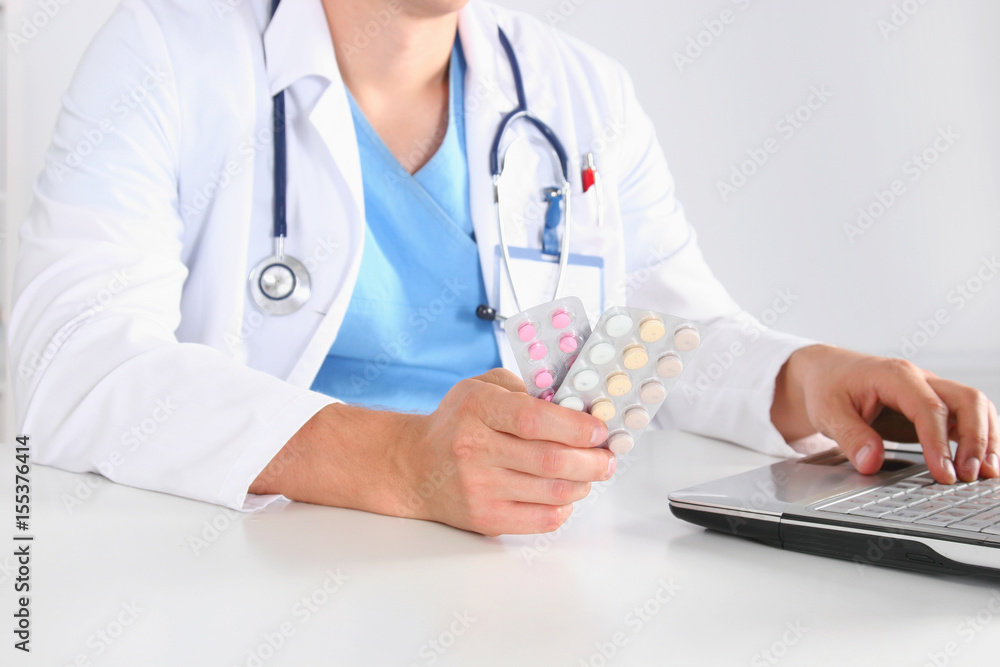 Male Doctor sitting at the table holding many different pills in his hand. Male Doctor sitting at the table holding many different pills in his hand.
