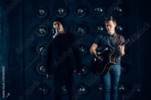 two musicians men's light and dark, guitarist, singer, fashionably dressed hipsters on stage, dark background, rock band, jazz, sing a song