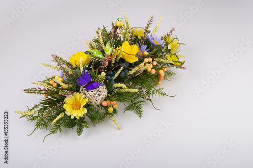 Colorful composition made of artificial flowers, fruits, butterflies, birds and ears of wheat in stylish vase on white background.