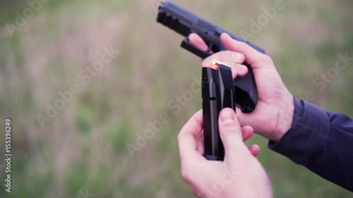 Male hand holding gun, reloading it and shooting from it on a field shooting