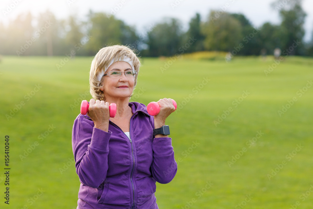 Mature woman doing exercises with dumbells at park in evening Mature woman doing exercises with dumbells at park in evening