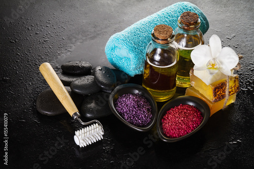 Beautiful Spa Set Spa Products with Essential Oils, Soap, Towel, Spa Sea Salt on Dark Wet Background. Horizontal with Copy Space.