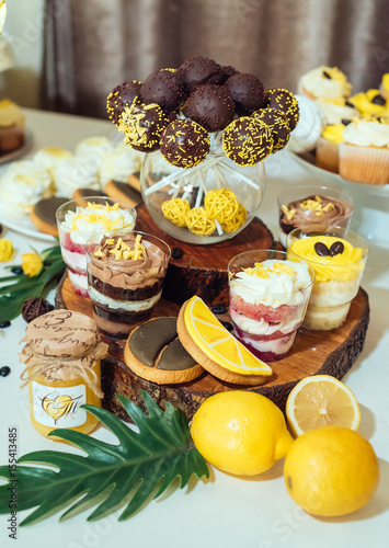 Chocolate cake pops, desserts in glasses and cookies on wedding candy bar. Holiday candy bar in yellow and brown color