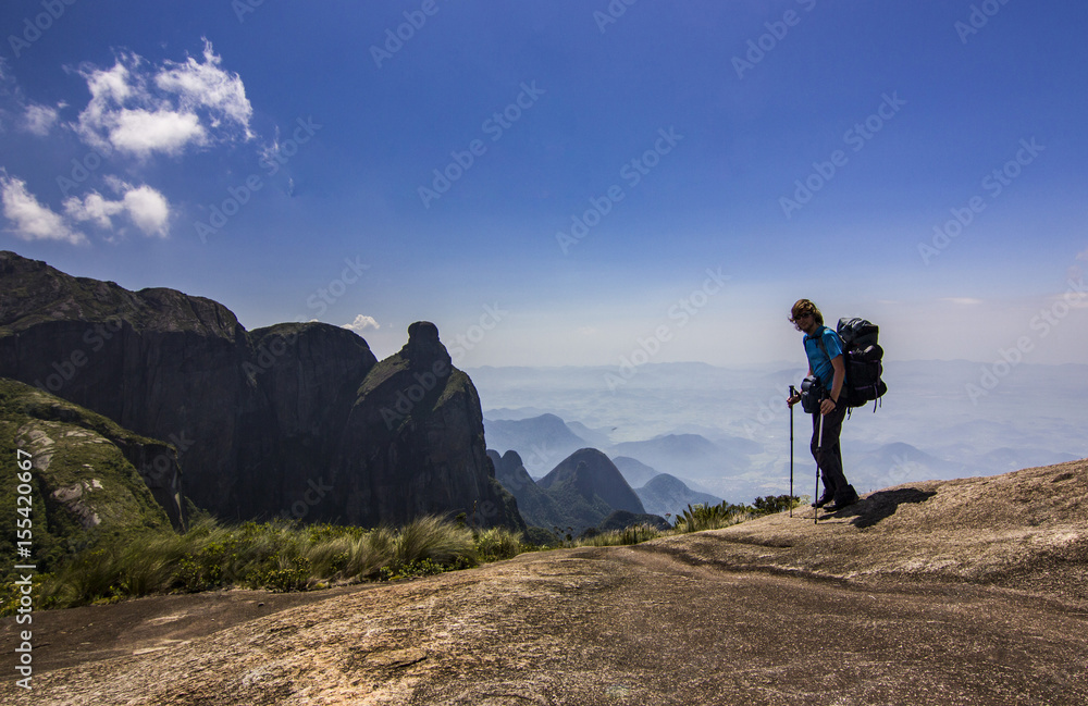 man with backpack standing on top of mountain with blue sky with clouds