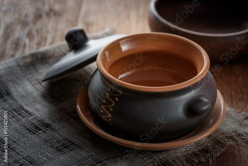 Clay pot for baking with lid on linen napkin on wooden background