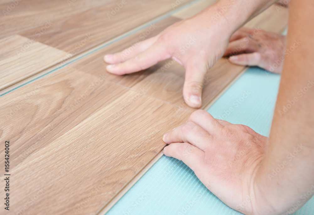Contractor installing wooden laminate flooring with insulation and soundproofing sheets. Man