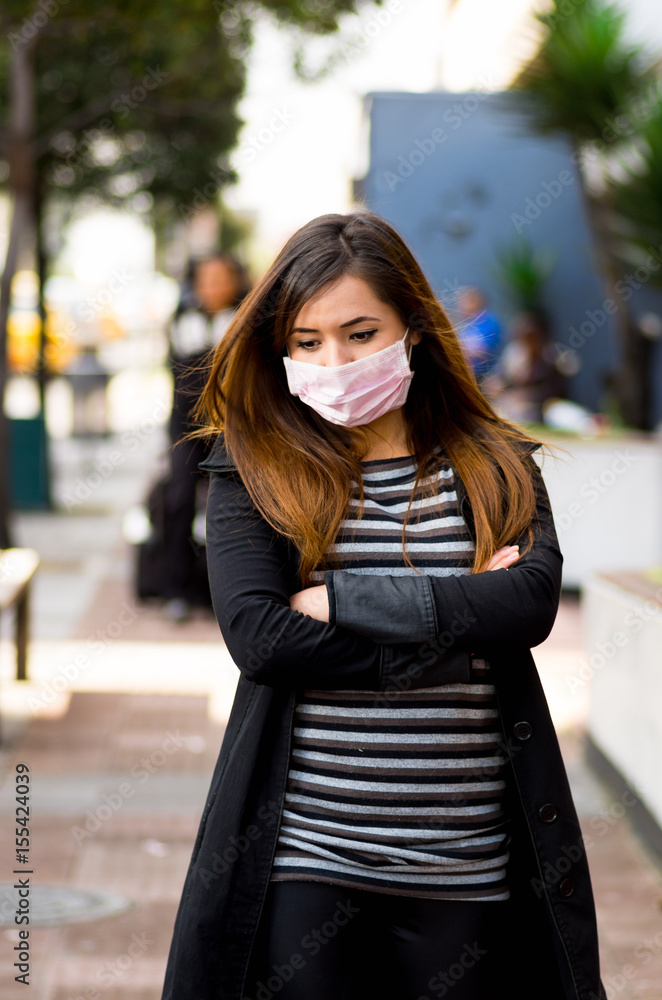 Sad young woman with protective mask feeling bad on the street in the city with air pollution, city background