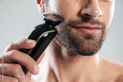Cropped image of a bearded man using electric razor photo