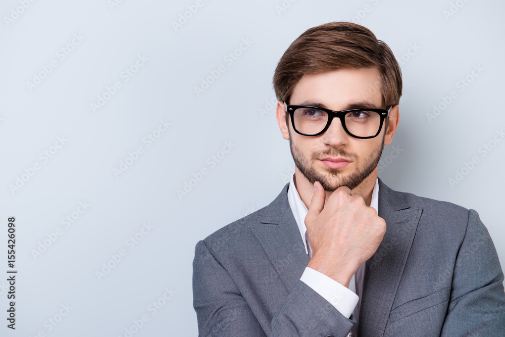Confident pensive handsome bearded young man is looking away wearing suit and glasses. touching his chin Confident pensive handsome bearded young man is looking away wearing suit and glasses. touching his chin