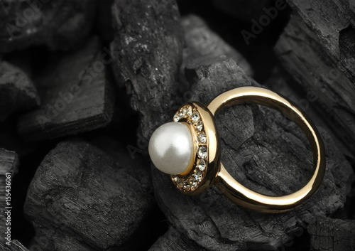 jewelry ring with diamond and pearl on black coal background, copy space