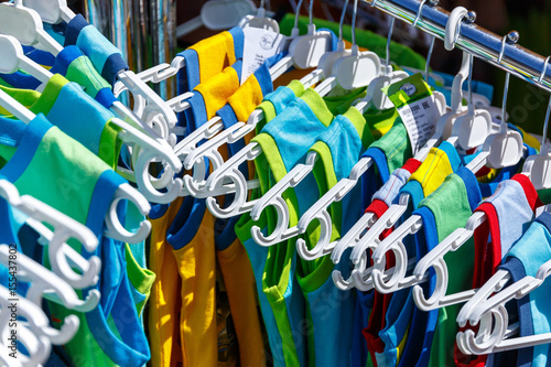 Baby clothes pants t-shirts sweaters shirts hanging on hangers in a shop outside in sunny weather photo