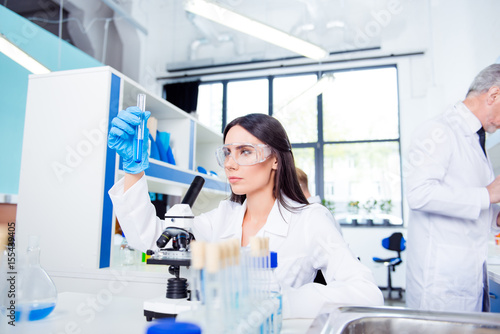 Laboratory, biotechnology, experiment. Young brunette cute intern is studying new technology in science, she is wearing labcoat and safety glasses, gloves