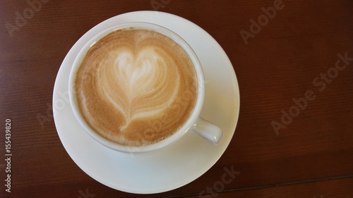 White cup with coffee and milk with drawings in form of heart on brown wooden background
