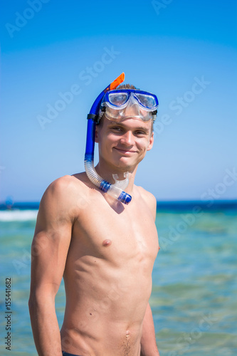 A young man stands and smiling near the sea in the mask for diving