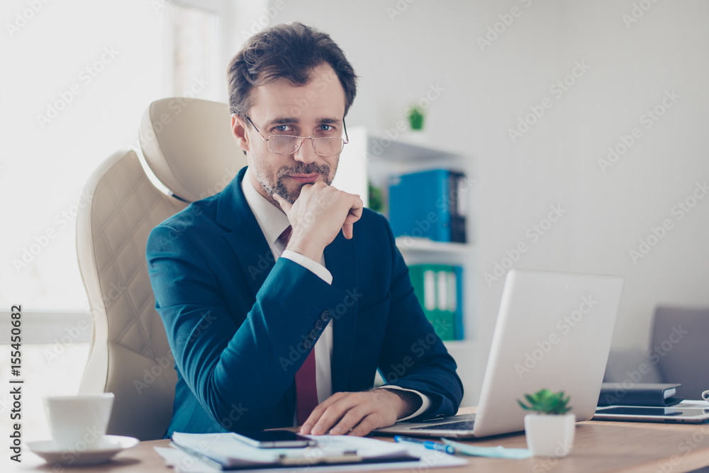 Smiling businessman banker is sitting at his workplace and looking in camera. He is wearing formalwear, glasses Smiling businessman banker is sitting at his workplace and looking in camera. He is wearing formalwear, glasses
