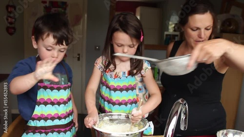Young family baking a cake in kitchen. Mum is heavily pregnant and teacher her son and daughter how to bake a cake on maternity leave