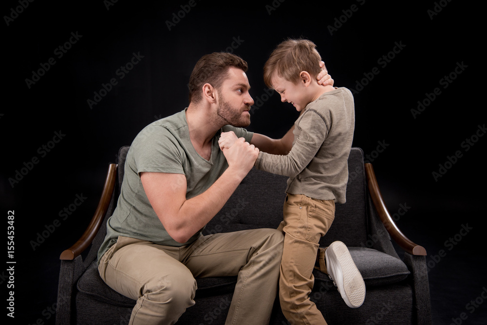 Angry father threatening to scared little boy isolated on black, family problems concept Angry father threatening to scared little boy isolated on black, family problems concept
