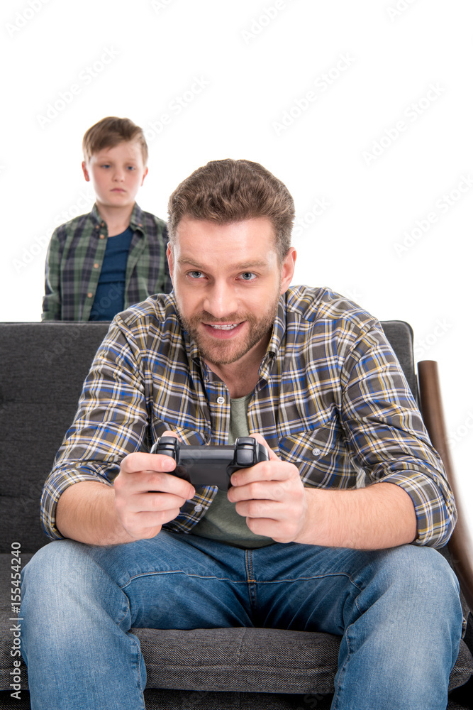 Little boy looking at father sitting on sofa and playing with joystick, family problems concept Little boy looking at father sitting on sofa and playing with joystick, family problems concept