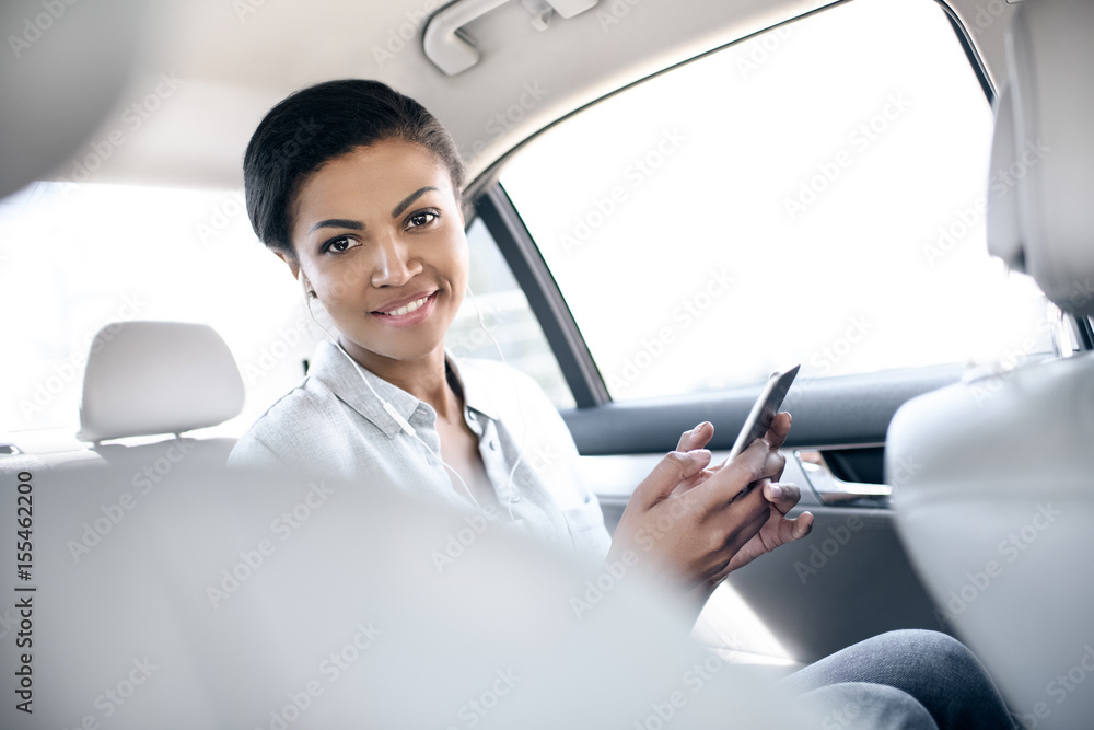 Beautiful smiling young woman sitting in car and using smartphone