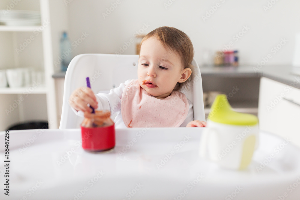 baby girl with spoon eating puree from jar at home baby girl with spoon eating puree from jar at home