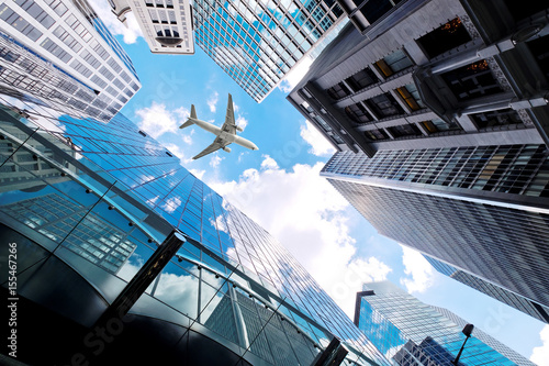Fotografie Airplane flying over business skyscrapers