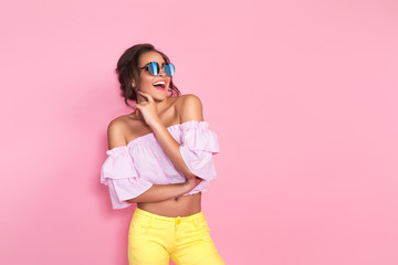 Beautiful girl in colorful clothes wearing sunglasses posing on pink background in studio.