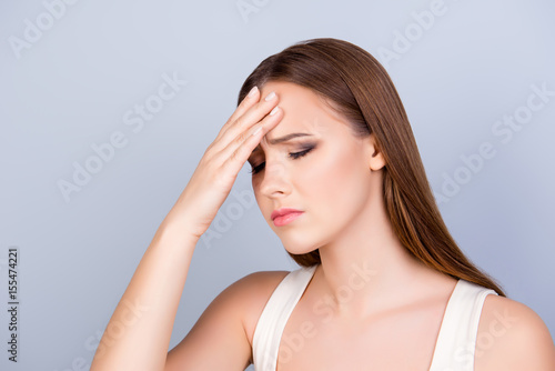 Exhausted young cute lady is touching her forehead with closed eyes, she is tired and depressed,, isolated on pure light background