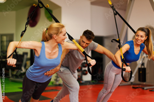 Personal trainer assisting young woman while exercising with trx in the gym