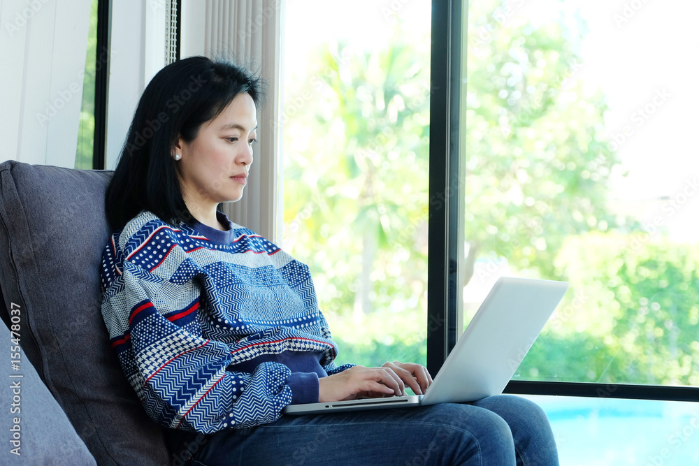 Asia woman using labtop computer while sitting on sofa at home background, technology and lifestyle concept Asia woman using labtop computer while sitting on sofa at home background, technology and lifestyle concept