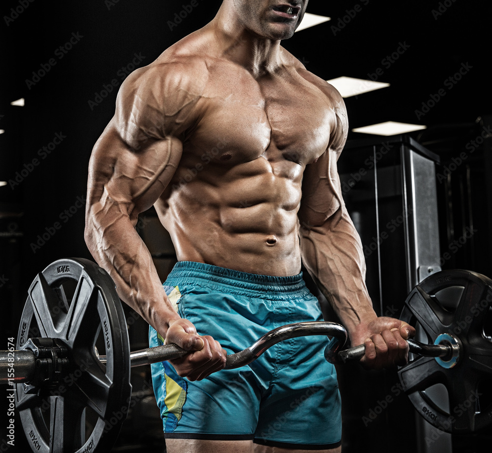 Fototapeta Przystojny mężczyzna z dużymi mięśniami, pozuje przy kamerą w gym