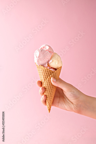 Leinwand Poster Woman hand holding an ice cream cone on a pink background.