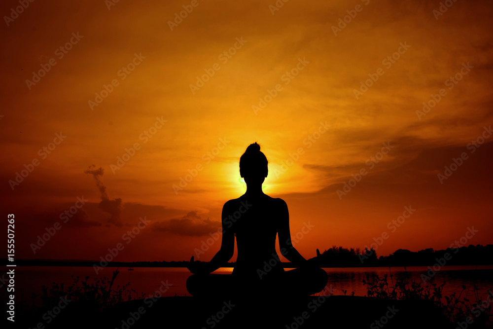 Young woman in a meditating yoga the beautiful sunset