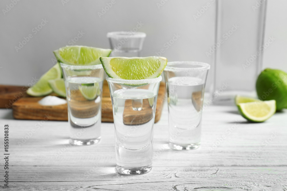 Tequila shots with juicy lime slices and salt on white wooden table Tequila shots with juicy lime slices and salt on white wooden table