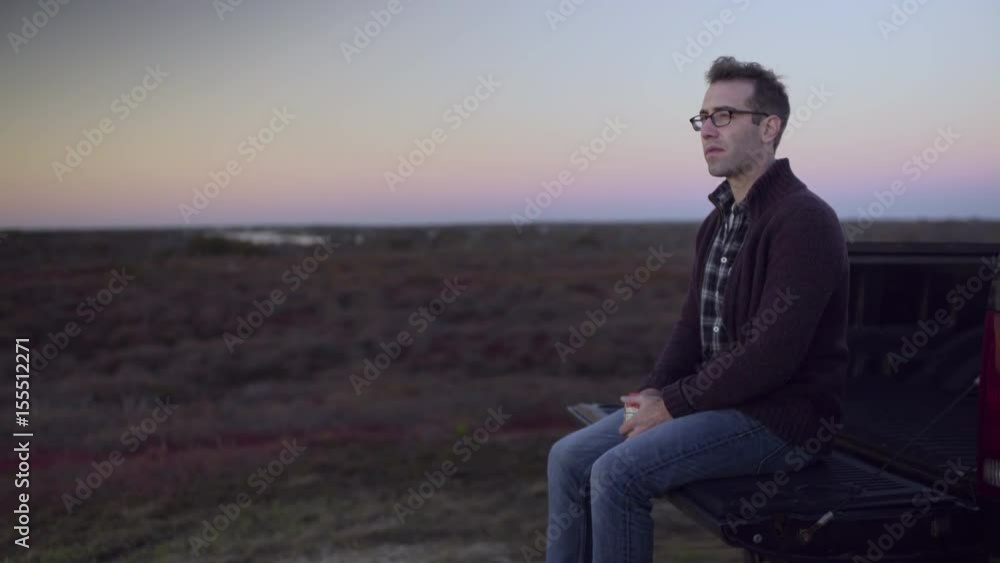 Man Sits On The Back Of His Truck, Eats A Snack And Watches The Sunset Man Sits On The Back Of His Truck, Eats A Snack And Watches The Sunset