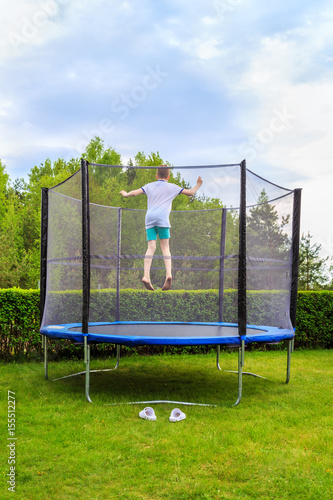 teen jumping on a trampoline against the backdrop of lush green of summer