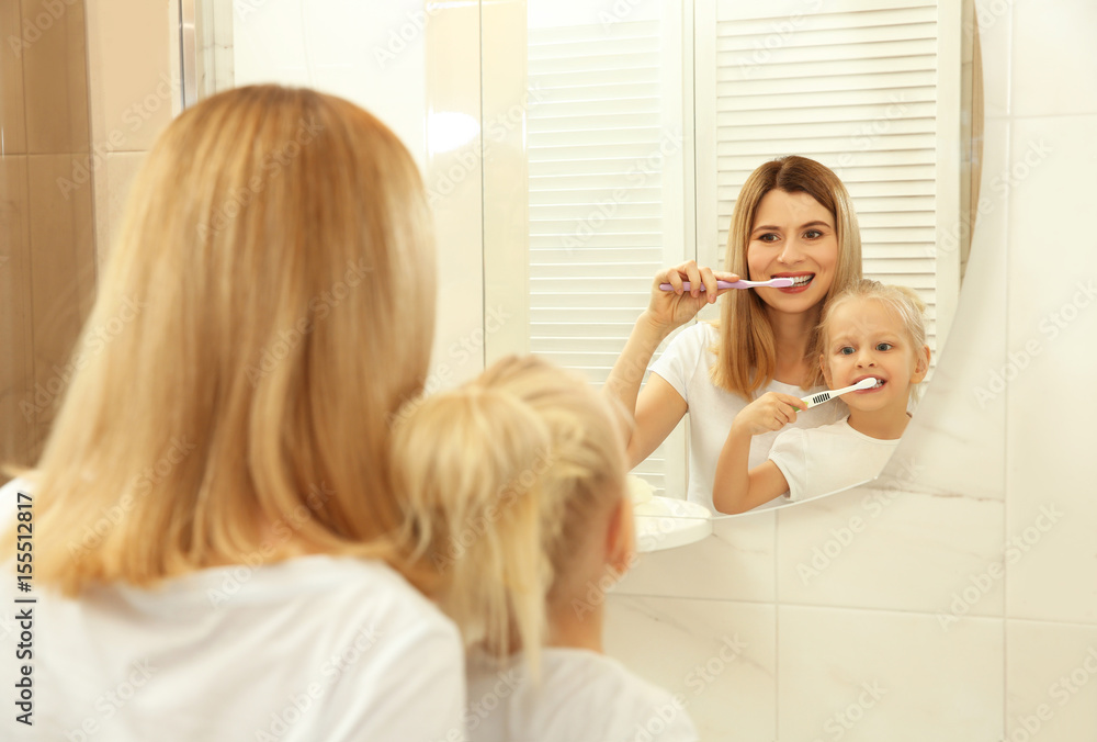 Young mother with her daughter brushing teeth and looking in mirror Young mother with her daughter brushing teeth and looking in mirror