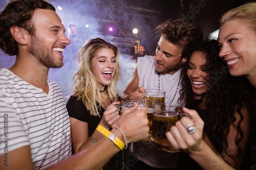 Happy friends toasting beer mugs at nightclub