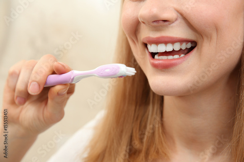 Smiling young woman with toothbrush on light background  close up