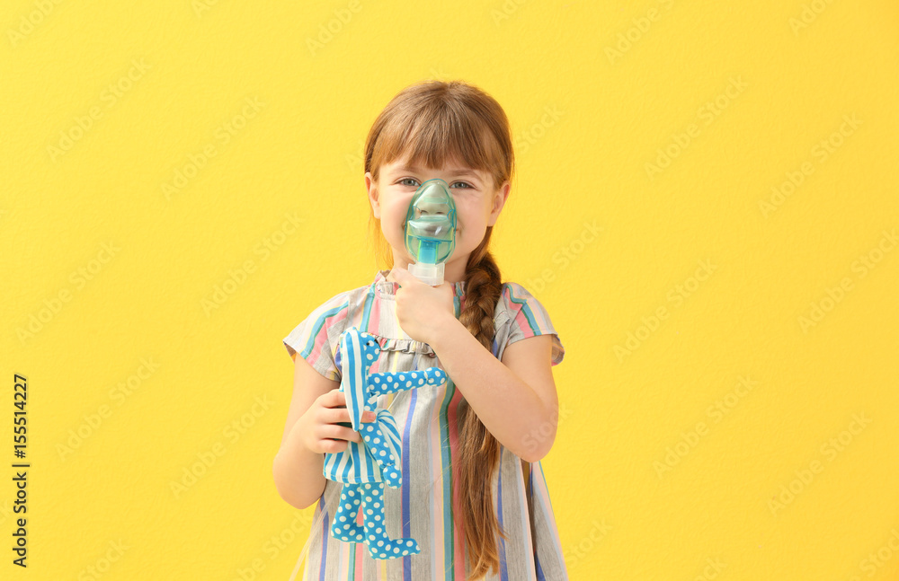 Cute little girl holding nebulizer and toy on color background. Allergy concept