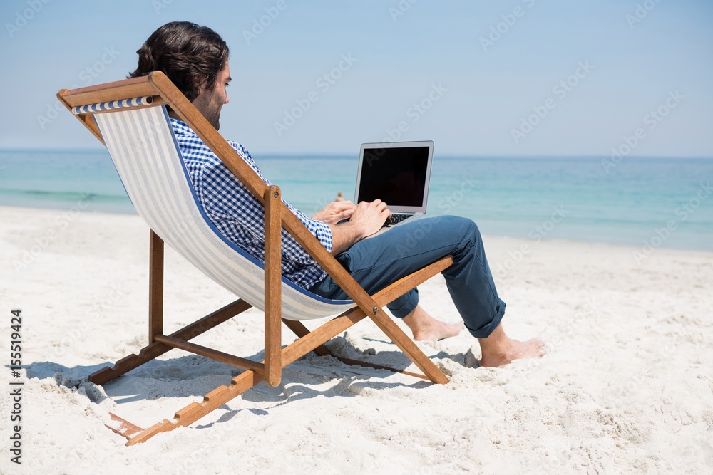 Side view of man using laptop at beach