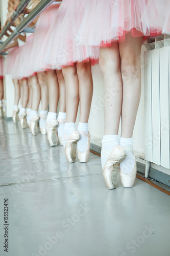 The close-up feet of a three young ballerinas in pointe shoes against the background of the wooden floor