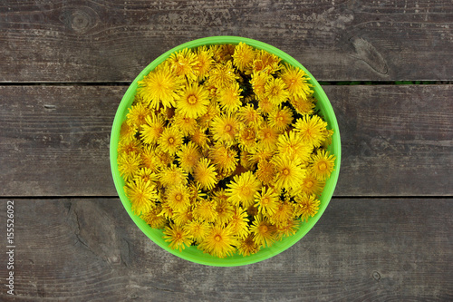 Fototapeta Naklejka Na Ścianę i Meble -  Green basket with yellow flowers of dandelions on the brown wooden background.