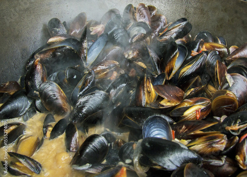 Fresh mussels at grill pan. Seafood barbecue outdoors. Picnic healthy food, mussels in shells. Plenty of mussel shells cooking at large metallic pan. Steamed and stewed mussels, mediterranean cuisine