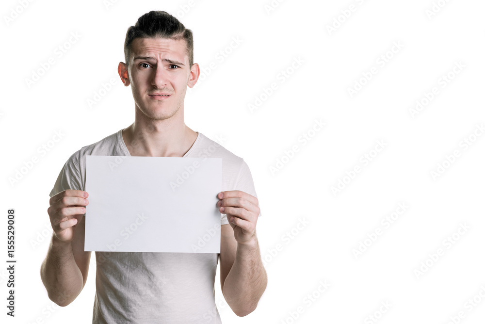 A young handsome guy with a blank sheet of paper, looking at the frame with perplexity. Place for signature, text. Horizontal frame A young handsome guy with a blank sheet of paper, looking at the frame with perplexity. Place for signature, text. Horizontal frame