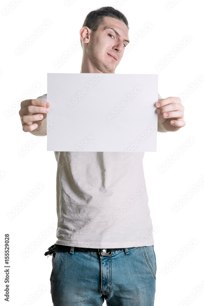 A young handsome guy with a blank sheet of paper looks at the sheet with disgust. Place for signature, text. Vertical frame A young handsome guy with a blank sheet of paper looks at the sheet with disgust. Place for signature, text. Vertical frame