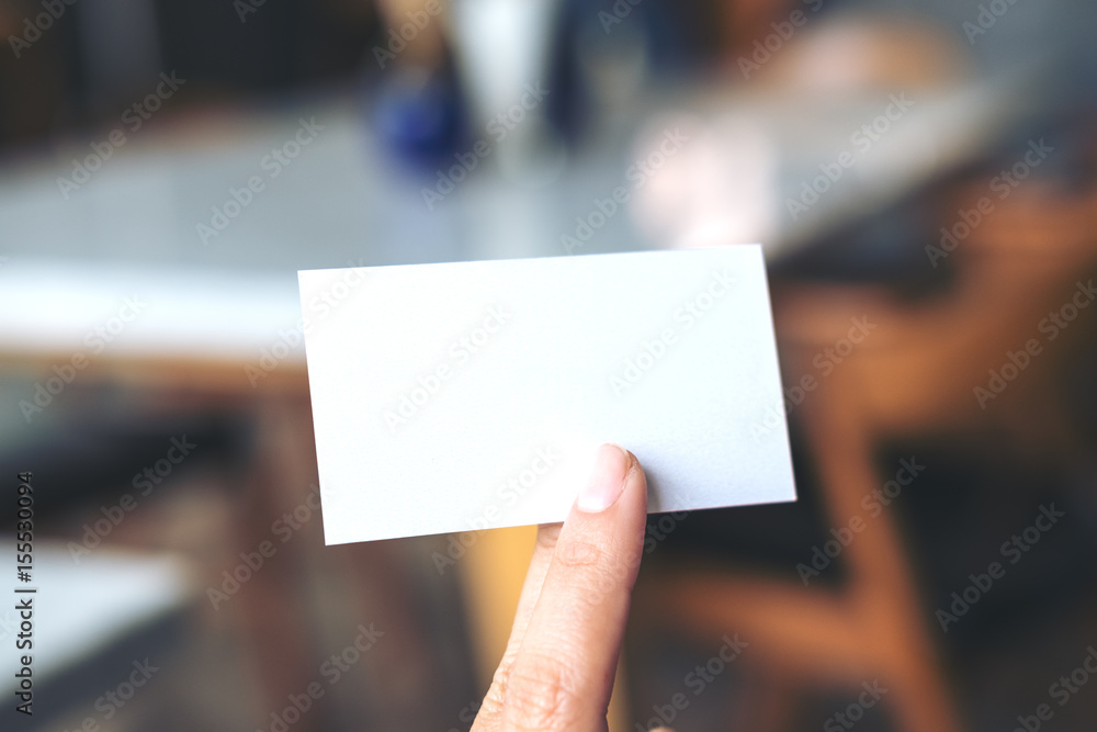 An image of a hand holding empty business card in modern cafe An image of a hand holding empty business card in modern cafe