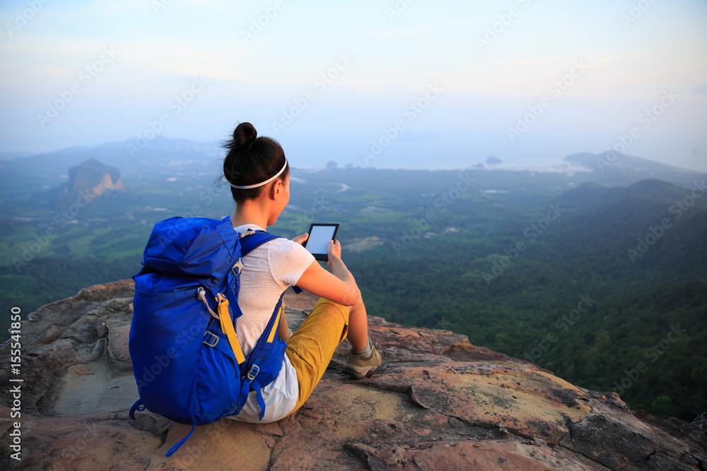successful woman hiker reading e-book on mountain top