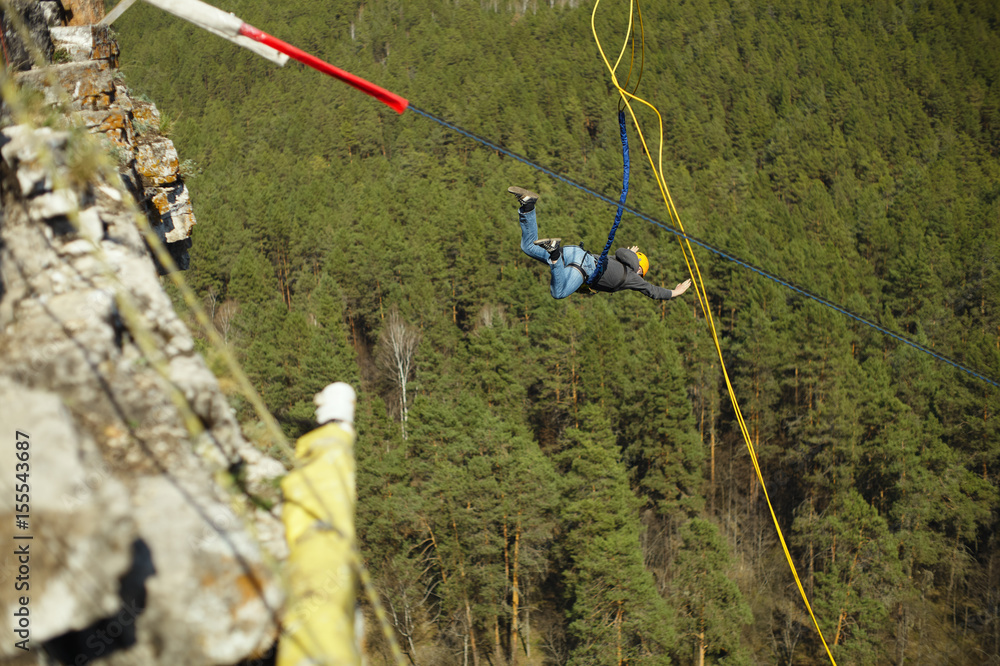 Obraz premium A man jumps into the abyss with a rope from a cliff.